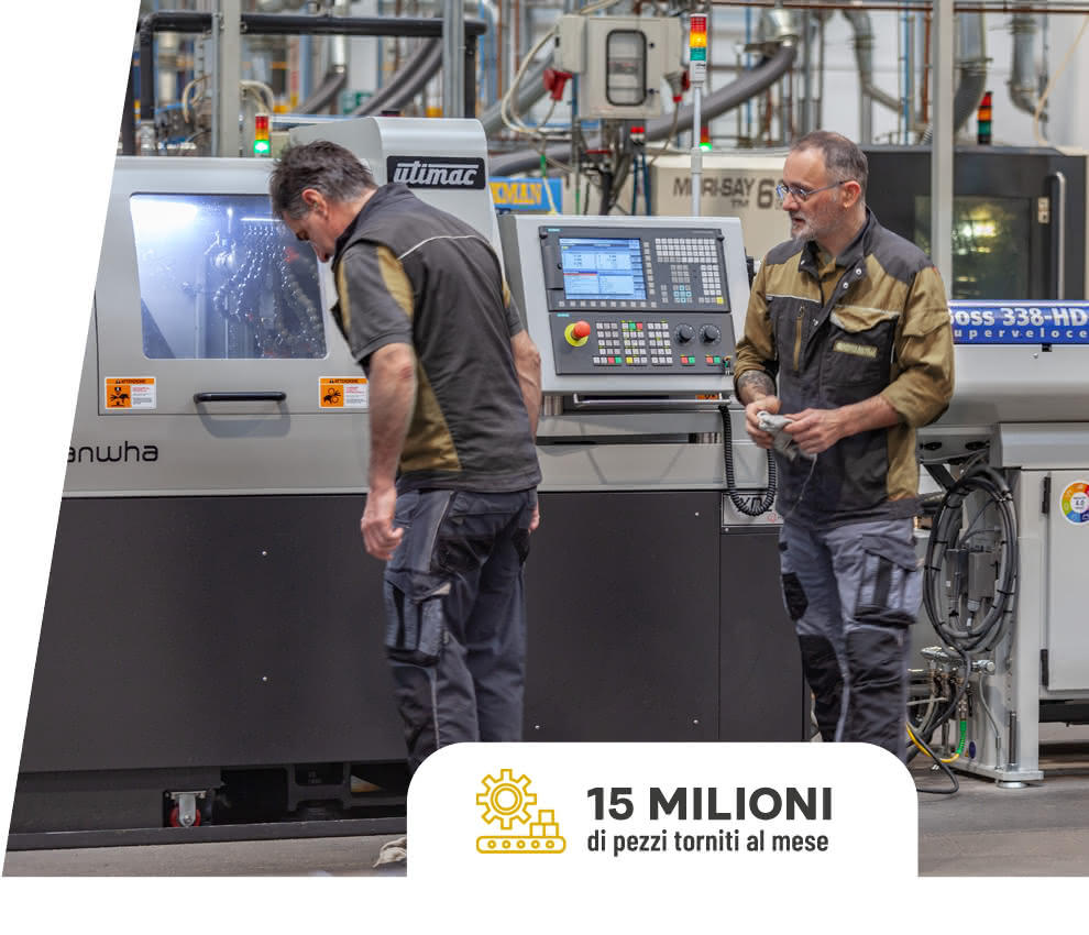 Due operatori Eredi Baitelli in fase di avviamento macchina su tornio CNC, con impianto produttivo visibile sullo sfondo.