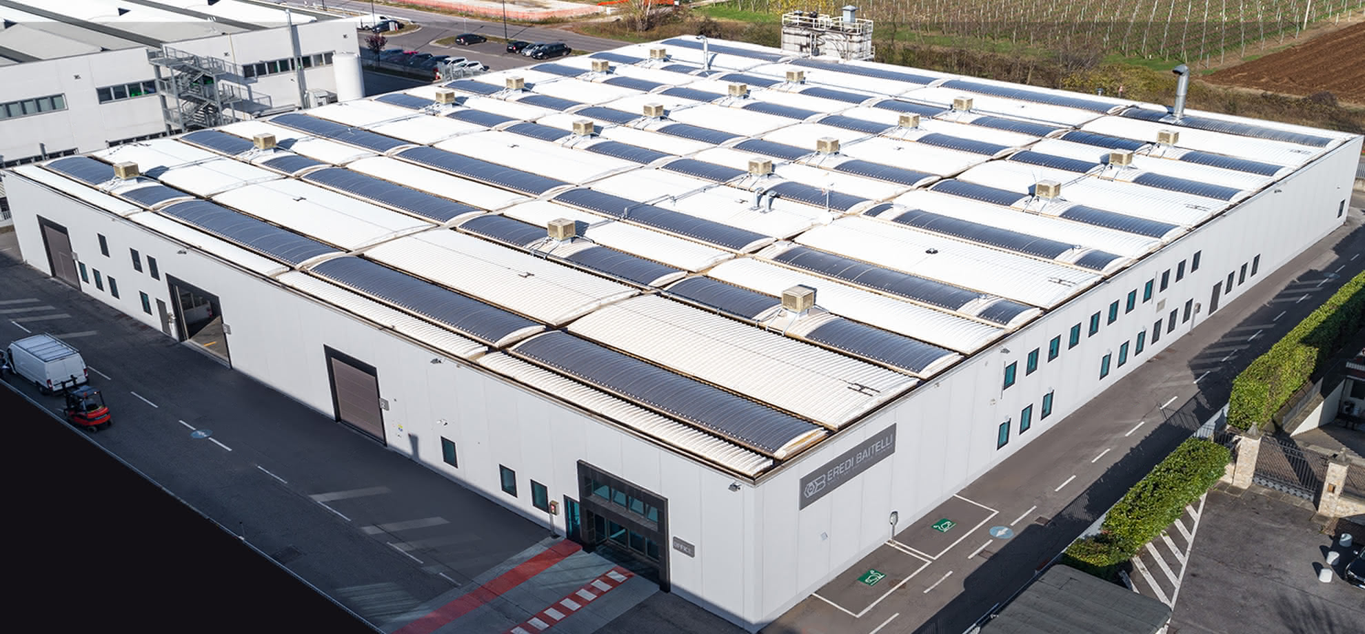 Veduta angolare dello stabilimento Eredi Baitelli con ingressi logistici, parcheggi dedicati e tetto a lucernari.