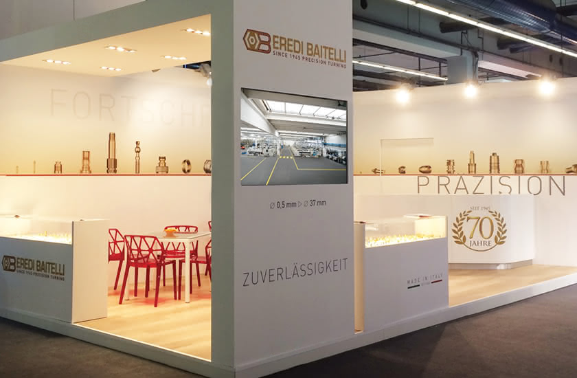 Stand espositivo di Eredi Baitelli in una fiera internazionale, con logo, campioni di minuteria e monitor multimediale.