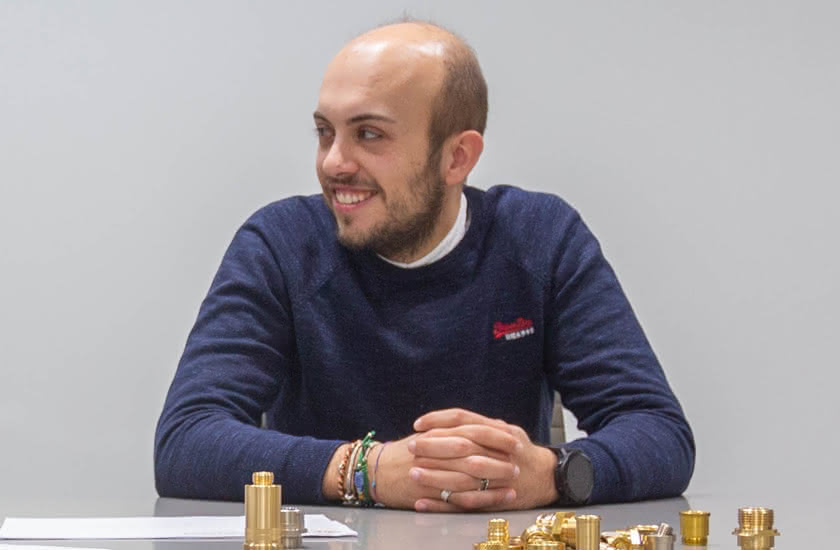 Matteo Baitelli seduto a un tavolo con componenti torniti in ottone davanti a sé, rappresentante della terza generazione aziendale.